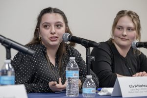 a young teenage girl talks into a microphone as a panelist sitting at a table