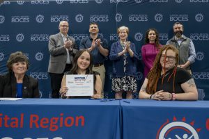 a young woman holds up a certificate sitting at a table with an adult woman