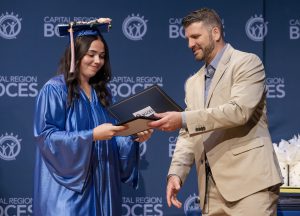 a girl wearing a blue cap and gown accepts an award from a man wearing a suit up on a stage