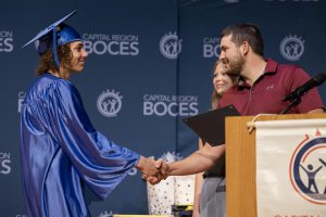 a young male graduate shakes the hand of an adult male on a stage