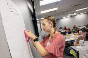 a young woman with braids in her hair sticks a post-it note on a while sheet