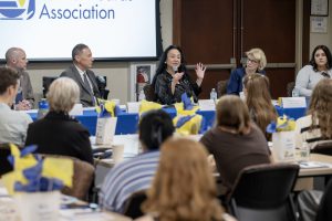 a panel of professional men and women sit at a table for a presentation