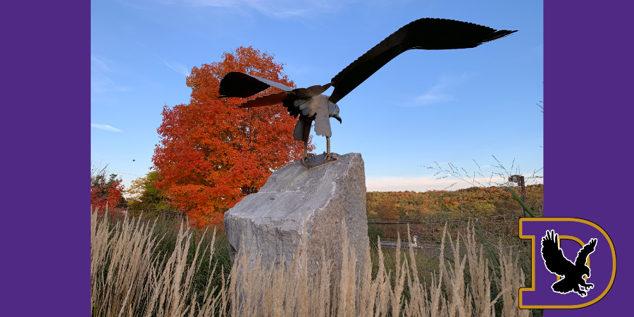 an eagle statue in front of a tree with orange leaves