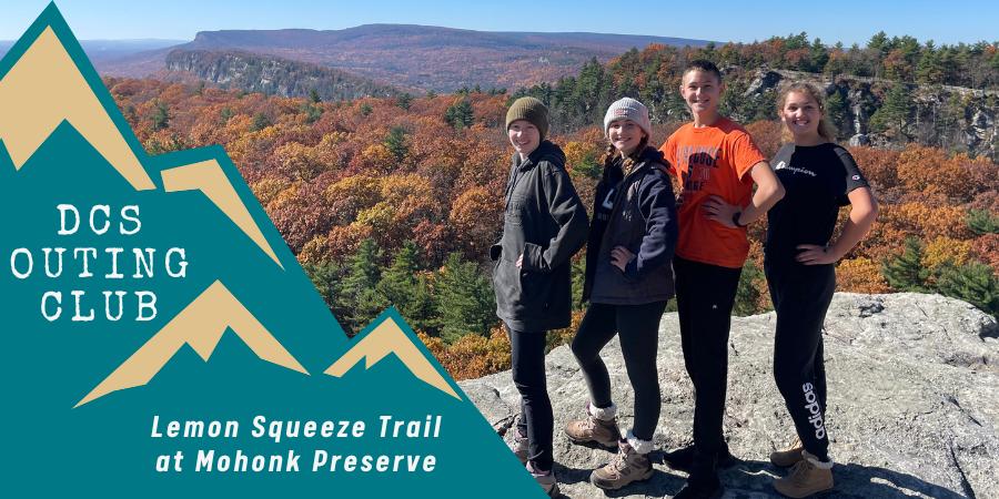 four teenagers stand on a rock ledge overlooking a mountain with fall colors