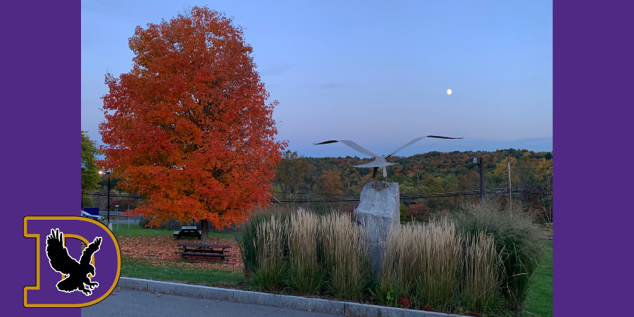 a statue of an eagle next to a tree with fall foliage