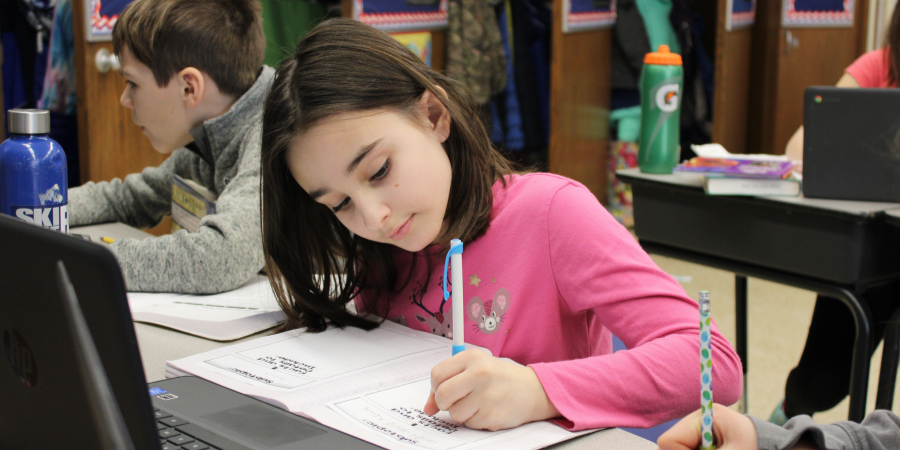 a young girl with a pink shirt handwrites a homework assignment