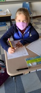 elementary student seated at desk while writing a letter