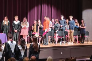 students participate in a ceremony on a stage in a school auditorium