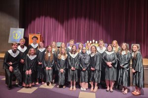 a group of students pose with black robes in front of a purple curtain in a school auditorium