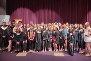 students pose in front of a purple curtain in a school auditorium