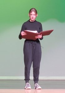 a young actress reads from a book on a theatrical stage