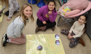 three young female students sit on the ground and participate in a coding exercise