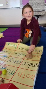 a young girl participates in a coding activity while sitting on a colorful carpet in a classroom