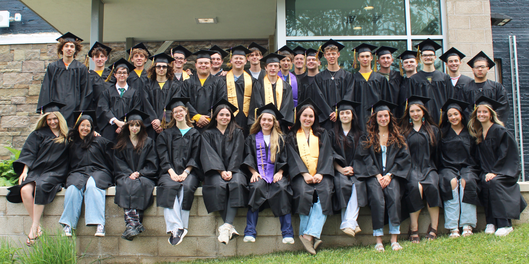students in caps and gowns pose in front of a school