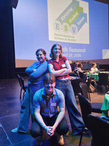 three students pose on a stage