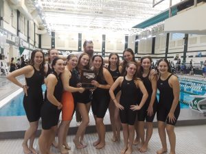 a group of female swimmers pose with a plaque in front of a pool