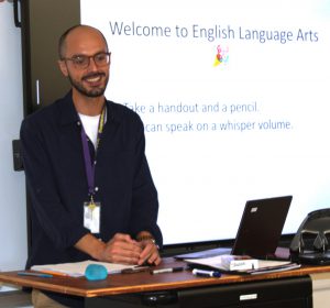 a bald man with glasses stands in front of a classroom teaching