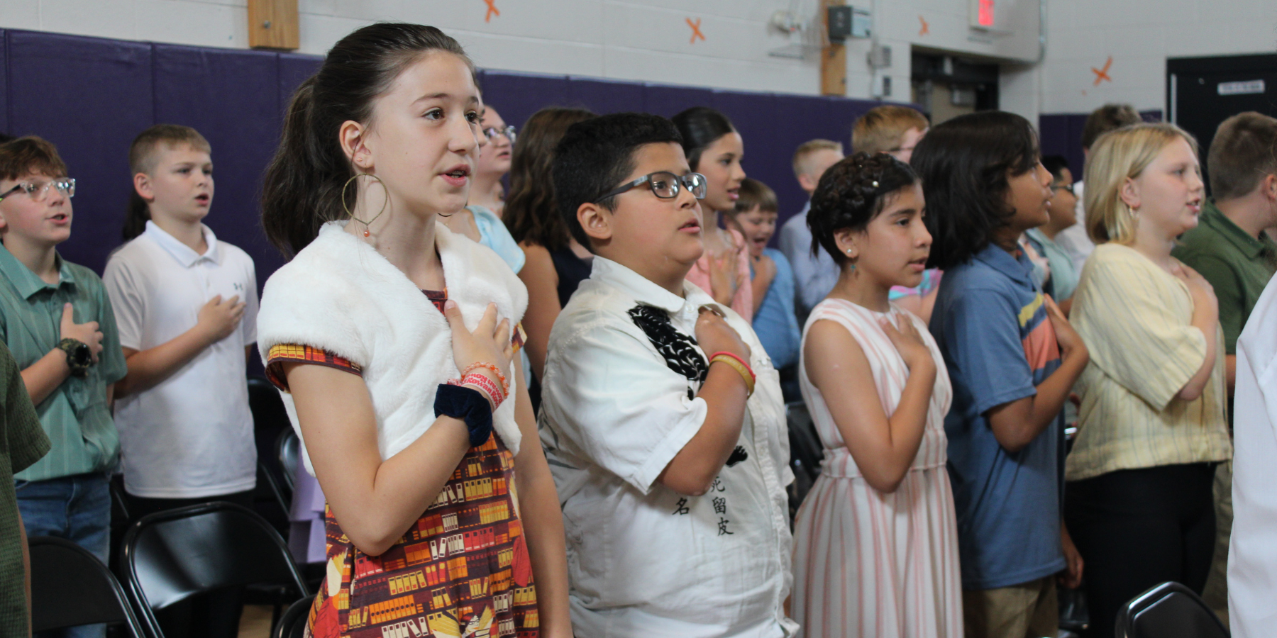 a group of young students hold their hands over their heart during the pledge of allegiance