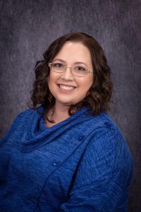 a woman with dark hair and glasses poses in a blue top