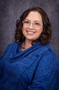 a woman with dark hair and glasses poses in a blue top
