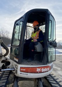 a young man wearing yellow and orange safety vest practices using a Bobcat