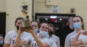 Basketball platers wearing white jerseys circle around one player holding up a trophy.