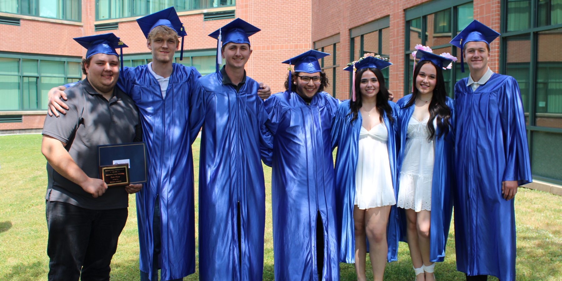 graduates in blue caps and gowns pose outside of a school