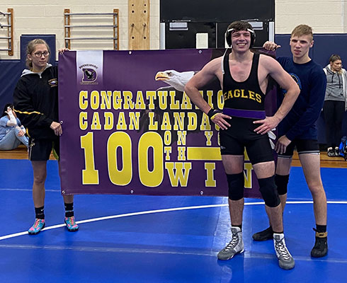 Cadan Landauer stands in front of 100th win banner