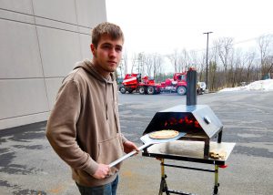 a young man takes a finished pizza out of a wood-fired oven