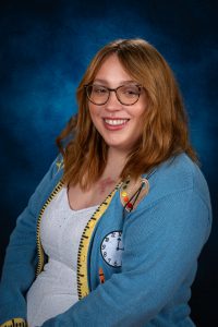 a woman with red hair wearing glasses, a white shirt and blue sweater