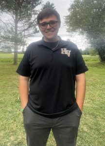 a man stands outside in front of trees wearing a black collared shirt