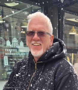 a man wearing a black winter jacket and glasses poses outside in the snow