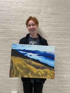 a teenaged girl holds a painting of an outdoor scene