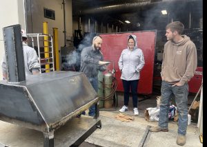 two adults and two students stand outside near a pizza oven