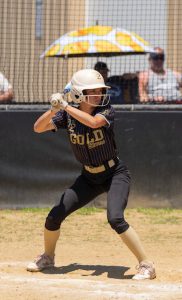 a young girl wearing a black uniform and helmet prepares to hit a ball with a bat