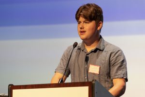 a young man stands at a podium and speaks into a microphone