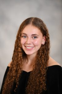 a girl with long brown curly hair poses for a senior portrait