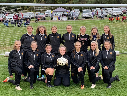 girls soccer team poses with ball on field