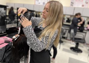 a young girl with blonde hair cuts the hair of someone sitting in a chair