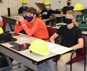 a young man with an orange shirt and a face mask sits at a table