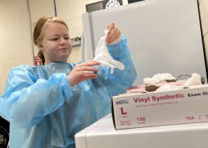 a young woman wearing blue scrubs puts on plastic gloves