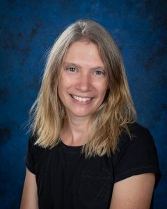 a woman with blonde hair, wearing a black t-shirt in front of a blue background