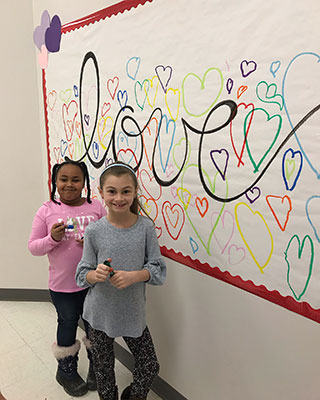 two students standing by hearts mural