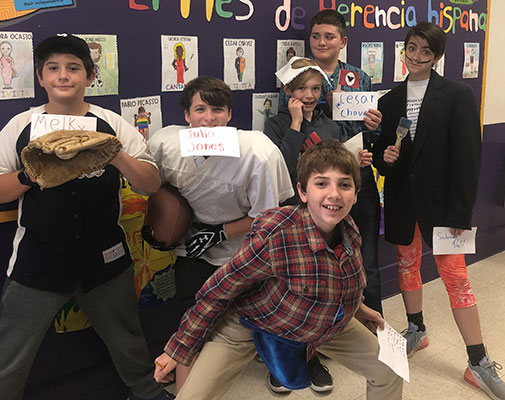 students holding cards with names of Hispanic Americans and standing in front of bulletin board