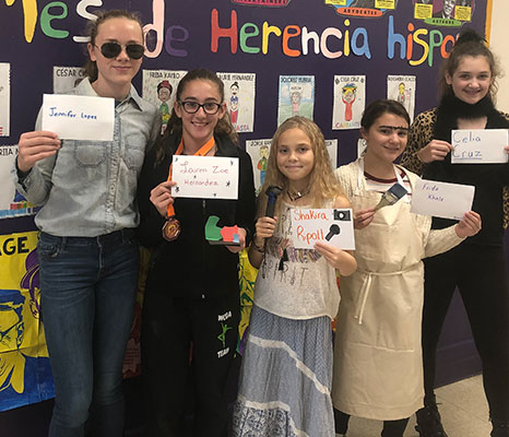 students holding cards with names of Hispanic Americans and standing in front of bulletin board