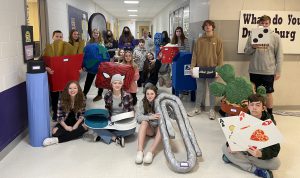 a group of students pose in the hallway of a school, holding their art projects