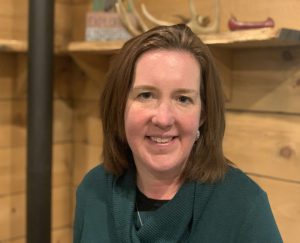 a woman wearing a green shirt poses in front of a wood wall