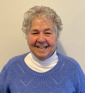 a woman with grey hair wearing a white turtle neck and blue sweater