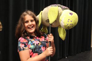 a girl smiles as she holds a fish prop while on stage
