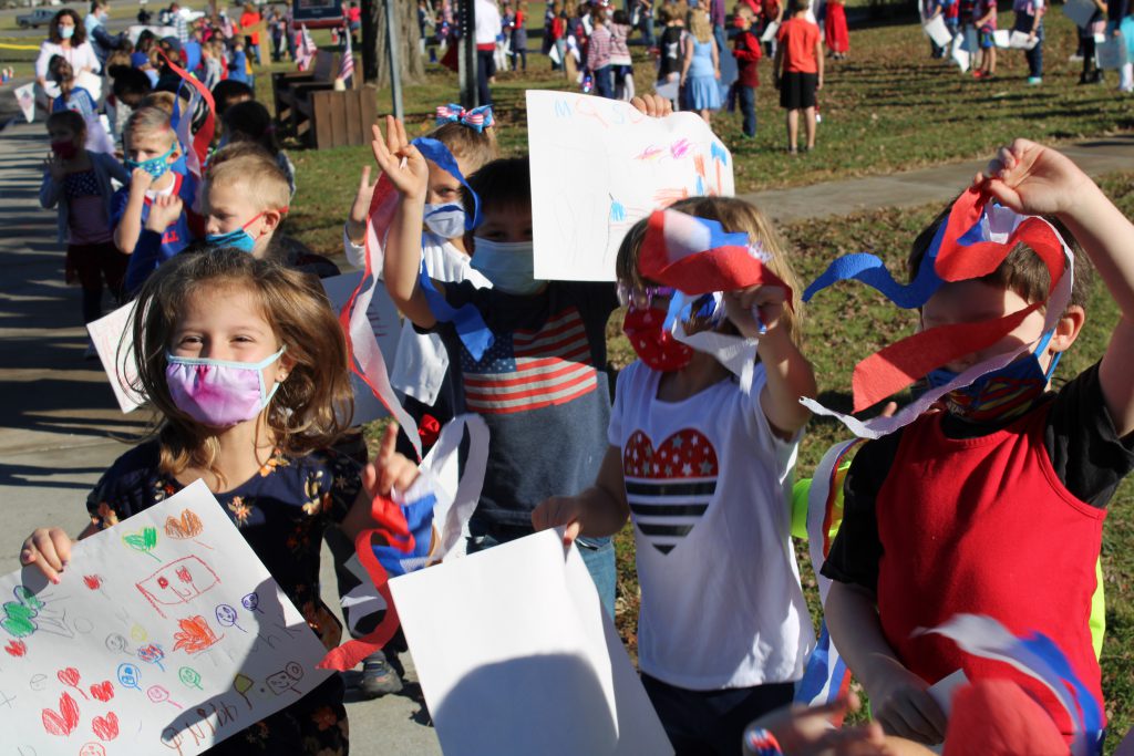 elementary students hold up signs in front of the school
